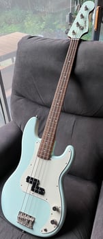 A teal colored electric bass guitar resting on a chair.