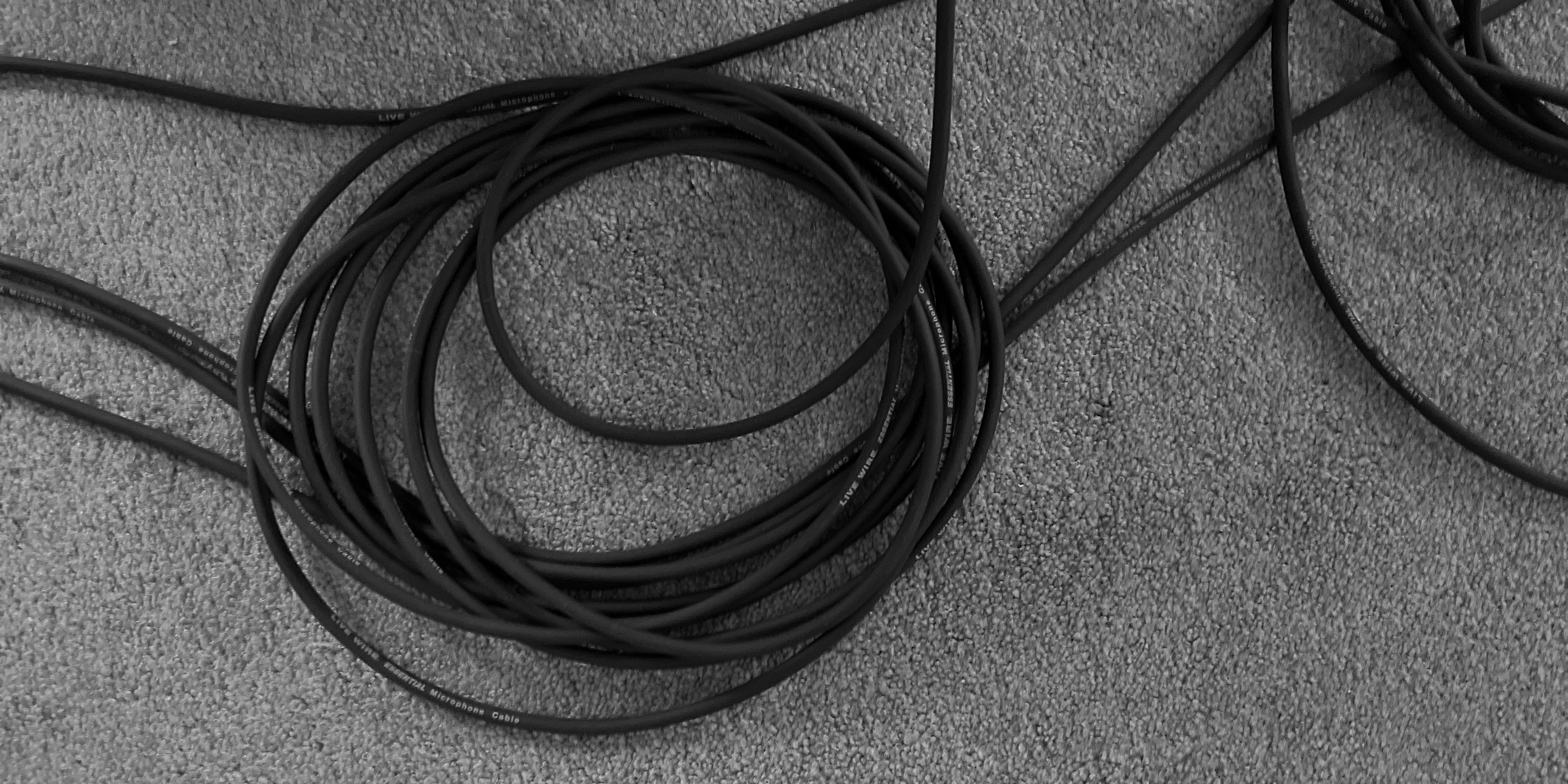 Aerial view of instrument cables coiled up on a carpeted floor in black and white.