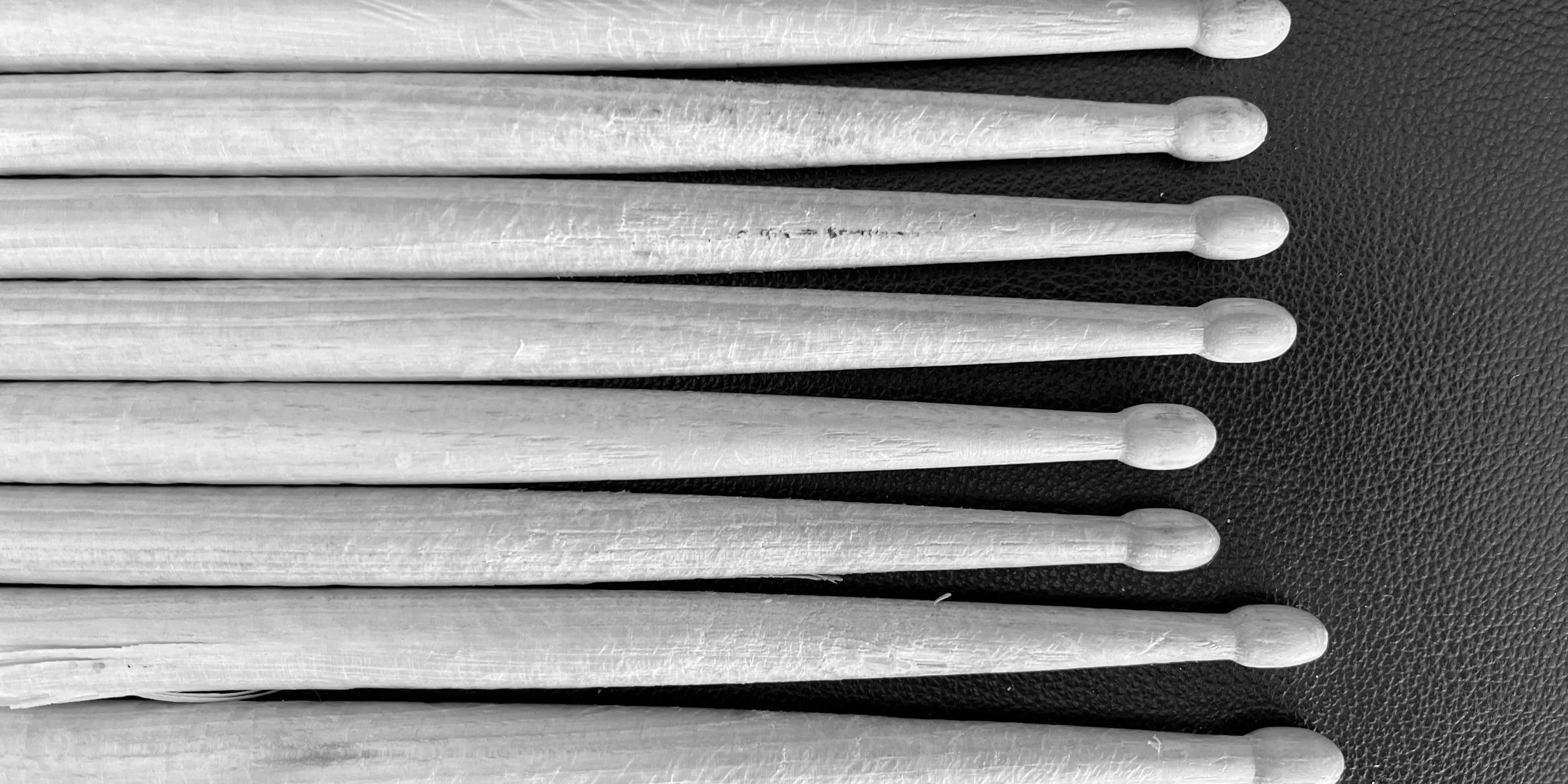 Drumsticks lined up next to each other pictured horizontally on a black background in grayscale