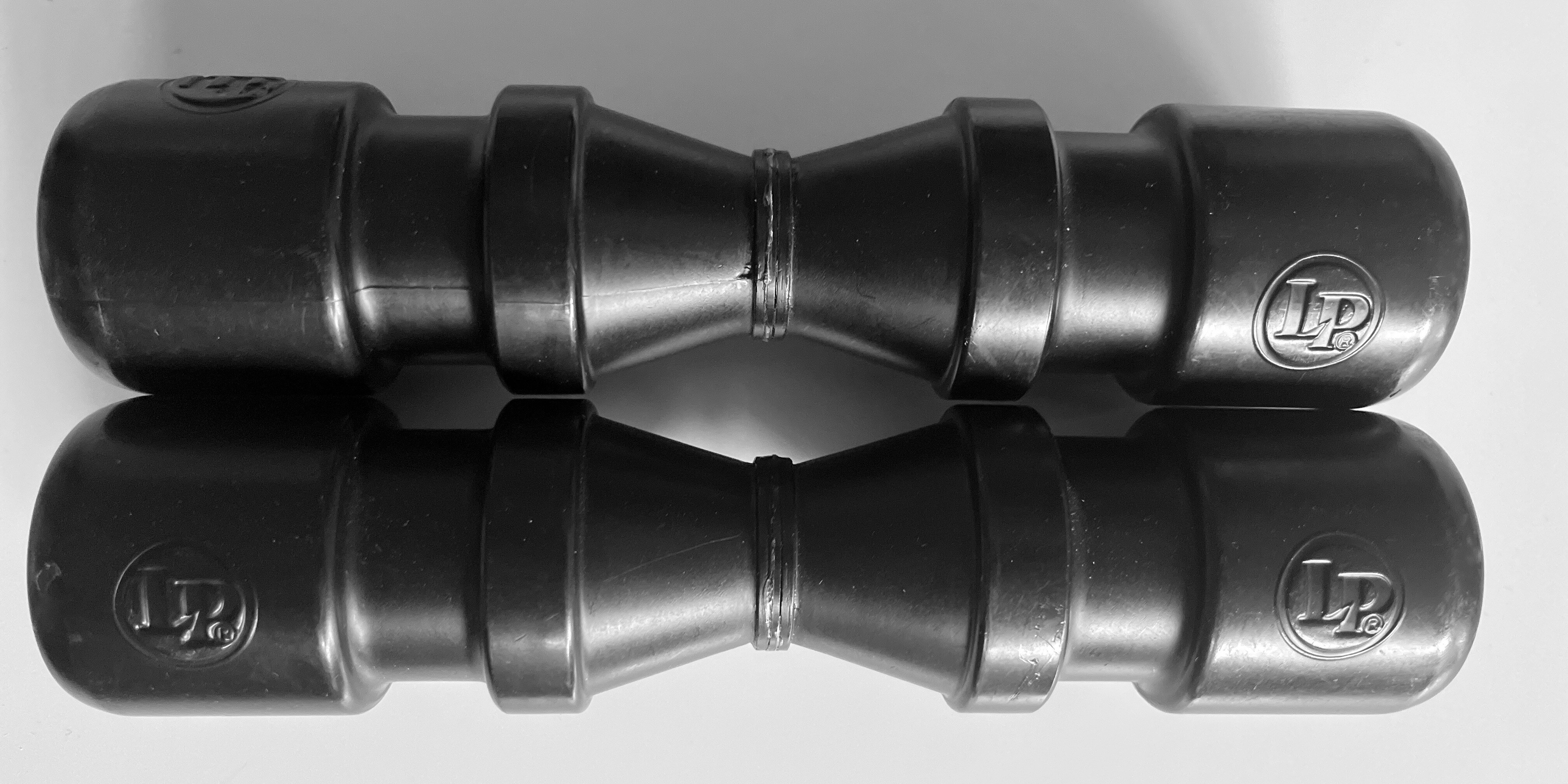 Two black LP brand shakers laying parallel to each other on a white table in black and white