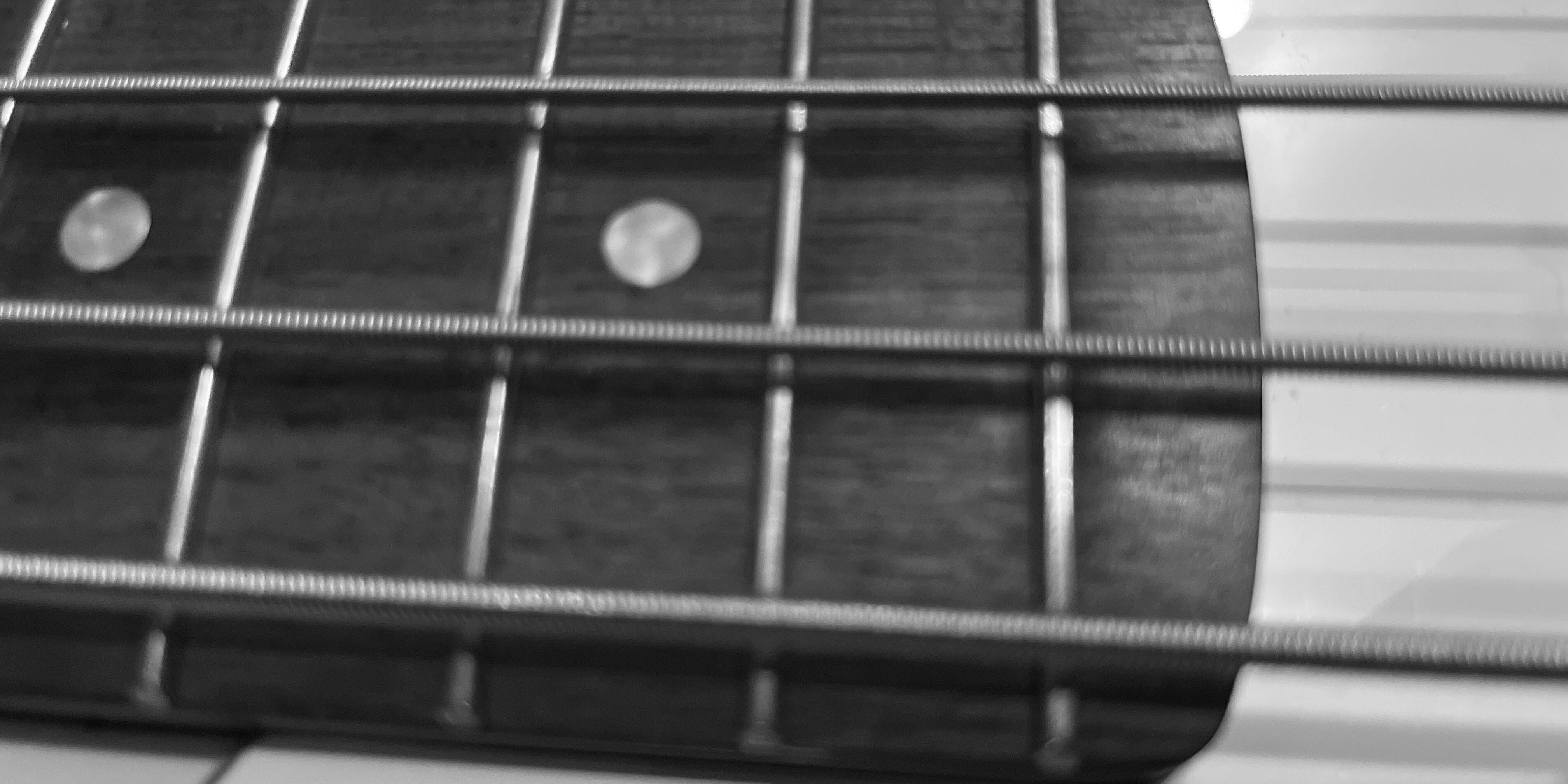 Black and white close-up image of the strings of a bass guitar over a fretboard.