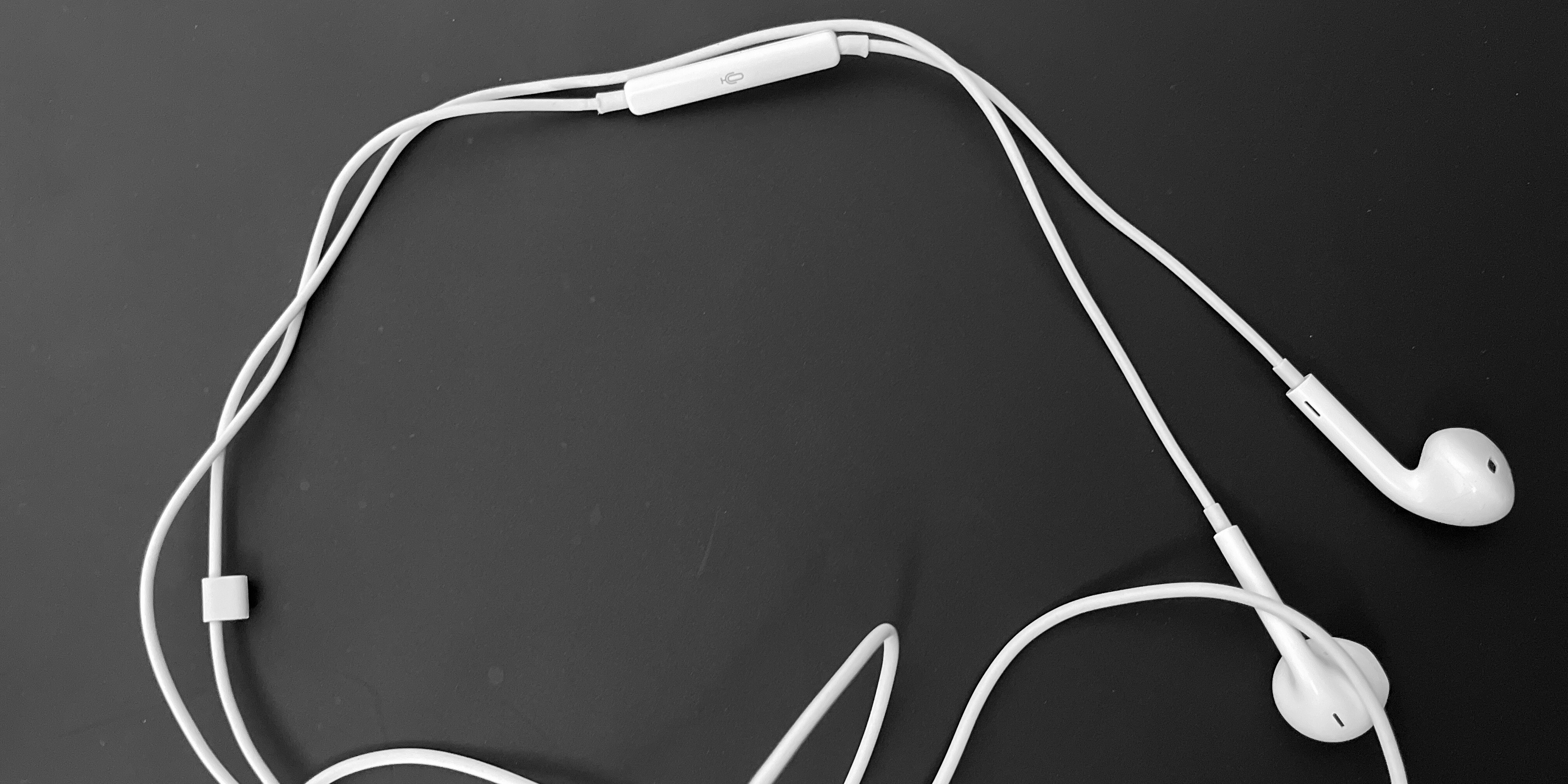 Black and white image of Apple wired earbud headphones sprawled out over a black background.