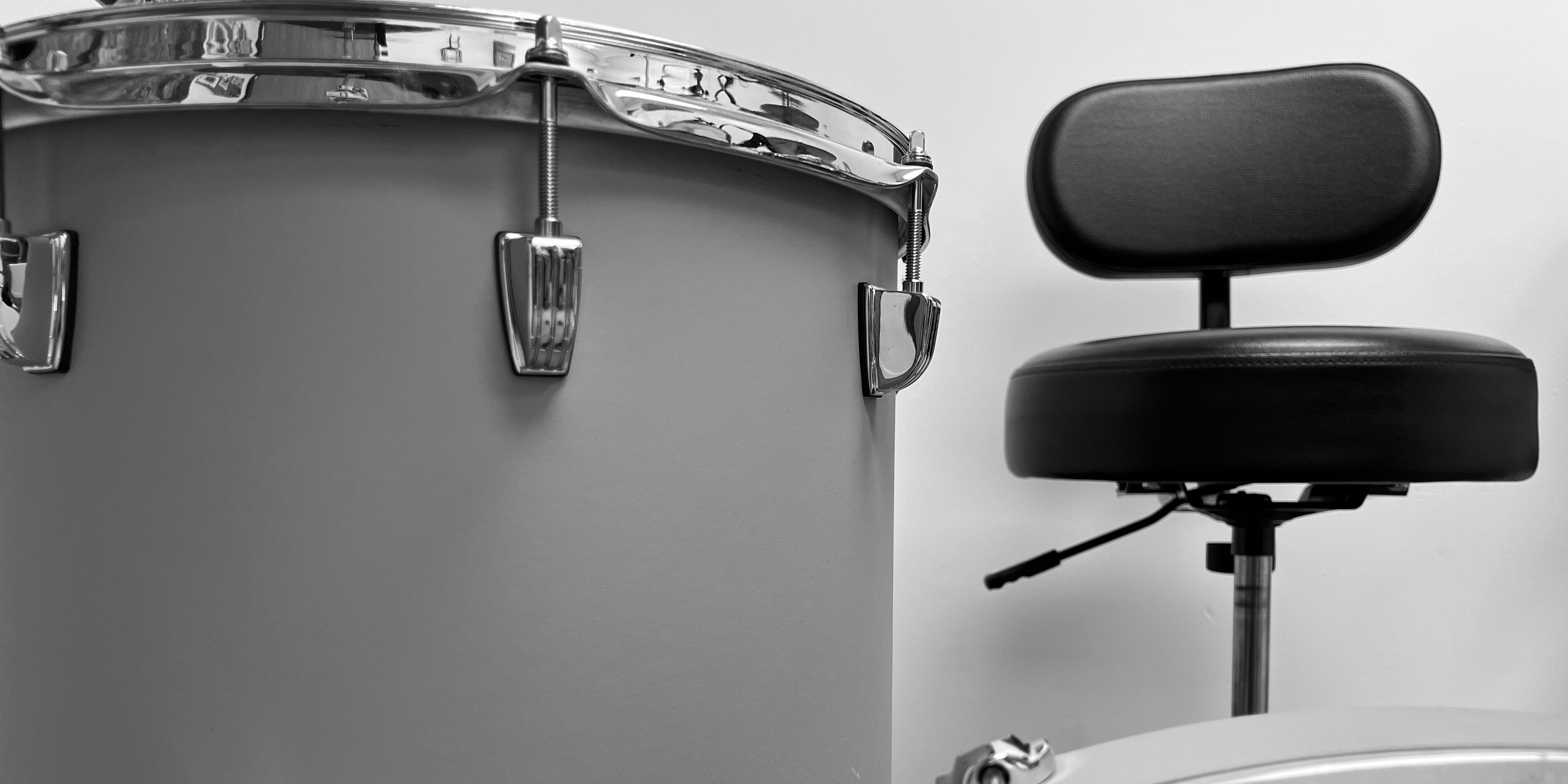 Black and white image of a floor tom and a drum throne as seen from a lens held directly over the front of a kick drum against a white wall