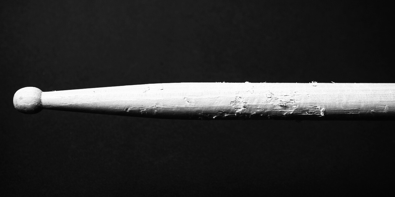 Black and white close up image of a drumstick on a black background. Image by StockSnap from Pixabay.