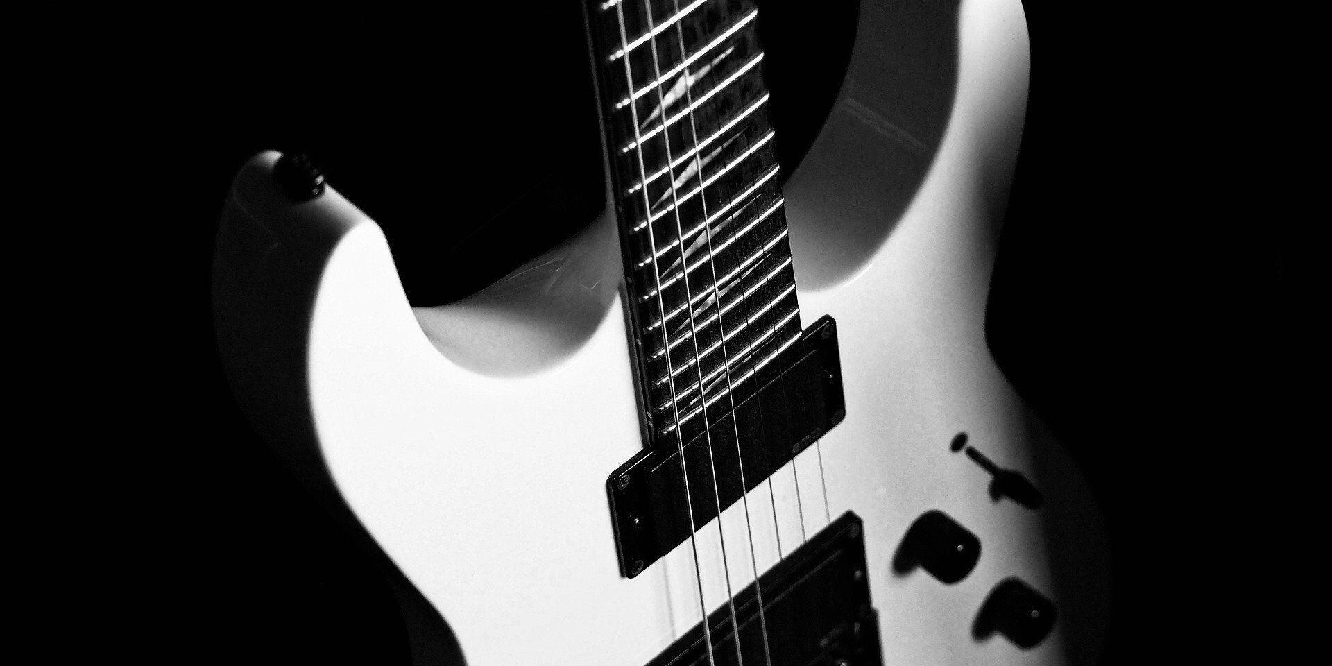 Image by Ralf Ruppert from Pixabay of a white electric guitar in front of a black background in grayscale